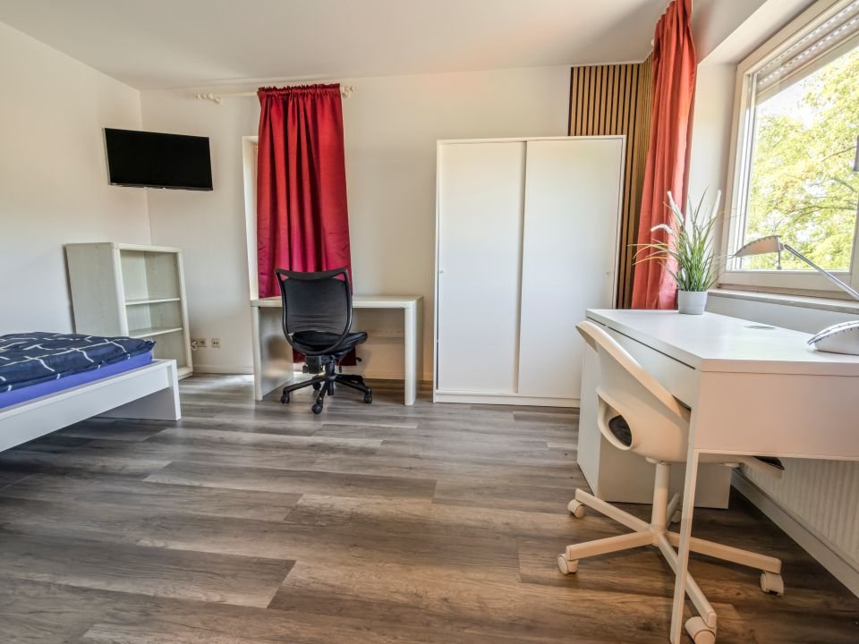 Quartier mit Bett, zwei Schreibtischen, Kleiderschrank und Wandfernseher